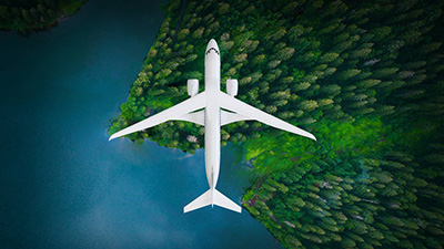 A top-down view of an experimental commercial aircraft flying above a forest next to a body of water to the left