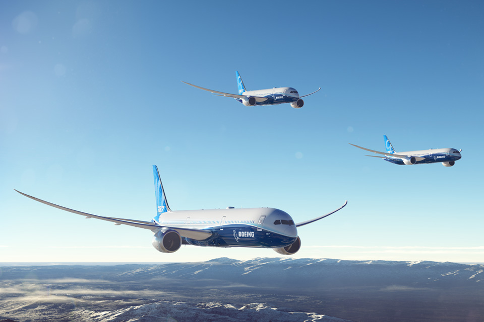 787 Dreamliner family flying together in clear blue sky over mountains.