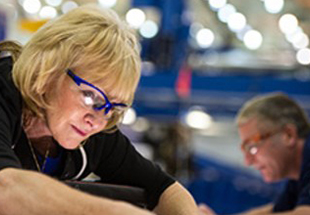 Two machinists collaborating on aircraft assembly, one person in the foreground and another machinist in the background. 