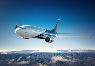 A Boeing 737 Boeing Business Jet flying above mountainous terrain against a clear sky.