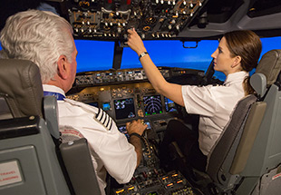 Two pilots in a flight deck simulator, actively managing the aircraft's controls and instruments during flight.