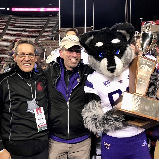 Craig Bomben, Steve Chisholm, and Harry the Husky with the Apple Cup.