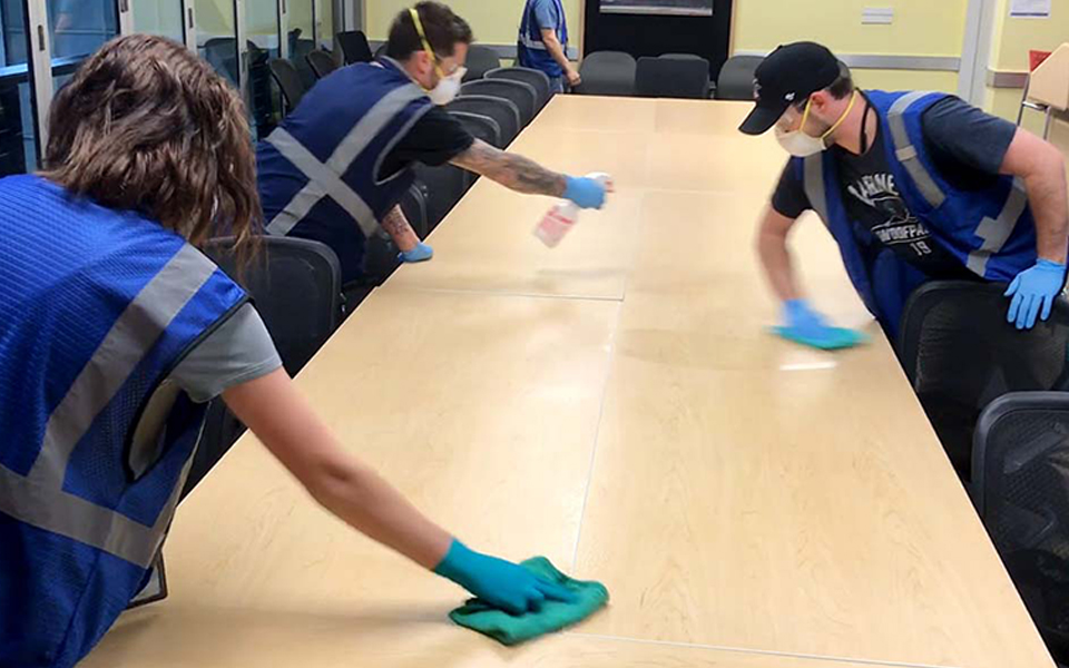 Boeing is committed to providing a clean environment, including more frequent cleaning of “high-touch” areas and common spaces. Here, blue-vested custodians clean a factory conference room.