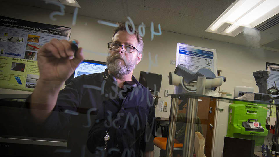 Boeing employee writing on clear board.