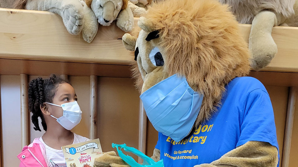 Child holding book and lion mascot, looking at each other
