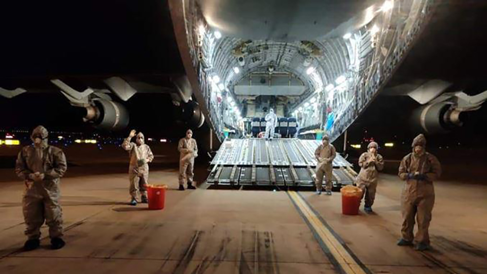 Crew members in personal protective equipment with open C-17 cargo bay 