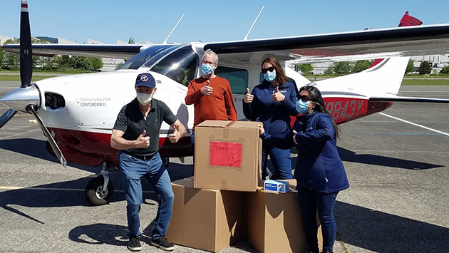Troy Larson (left) and three Washington State Hospital Association teammates in front of an airplane with a box of equipment 