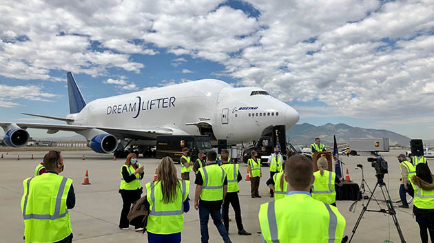 Boeing Dreamlifter in back of people in yellow safety vests