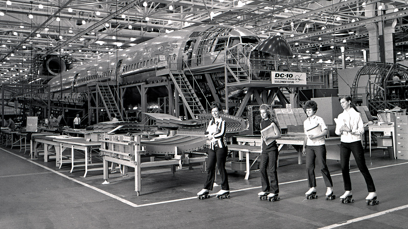 Black and white photo of women roller skating through aircraft plant.