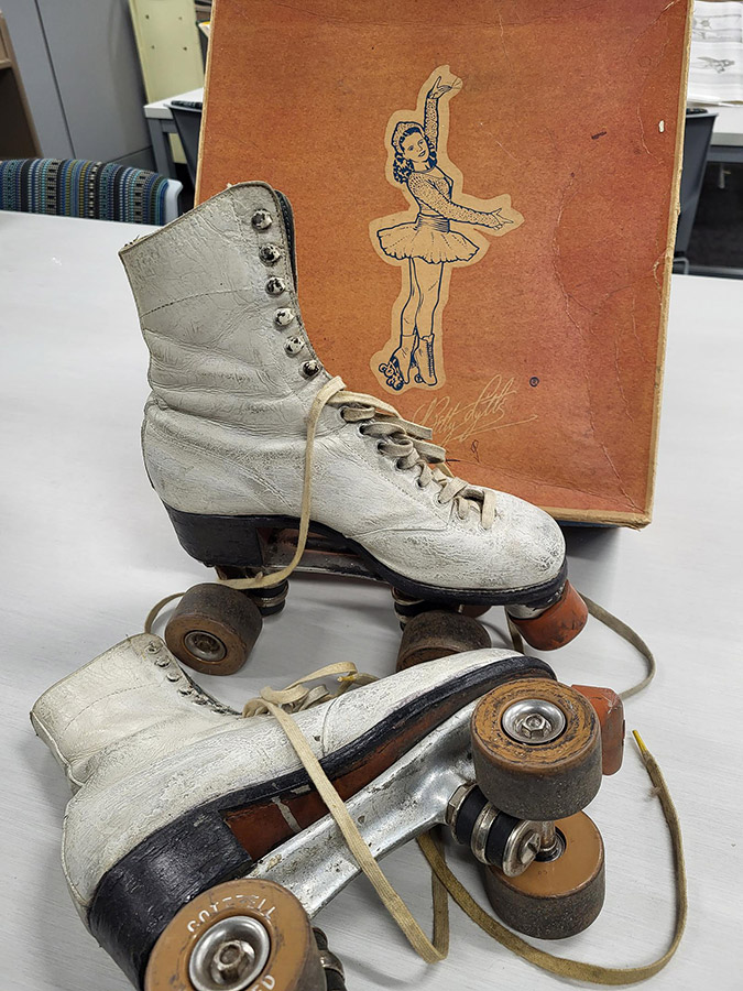 Color photo of white vintage roller skates sitting on table.
