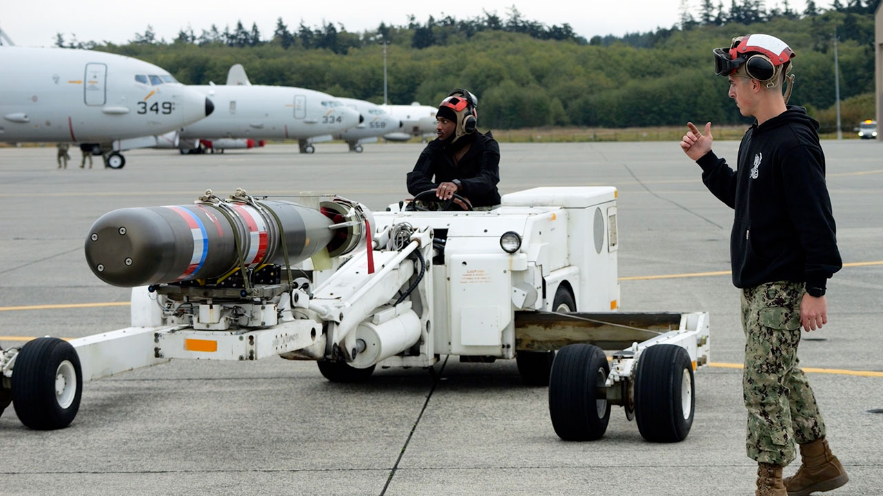 Aviation ordnancemen deliver an inert training torpedo to a P-8A Poseidon on the NAS Whidbey Island flight line.