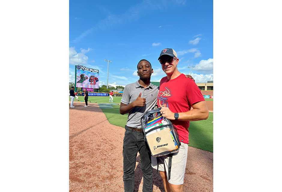 In Jacksonville, Florida, a Boeing employee gives a backpack full of school supplies to a local high school student who threw out the first pitch at a Jacksonville Jumbo Shrimp baseball game, bringing awareness to chronic student absenteeism in Duval County.