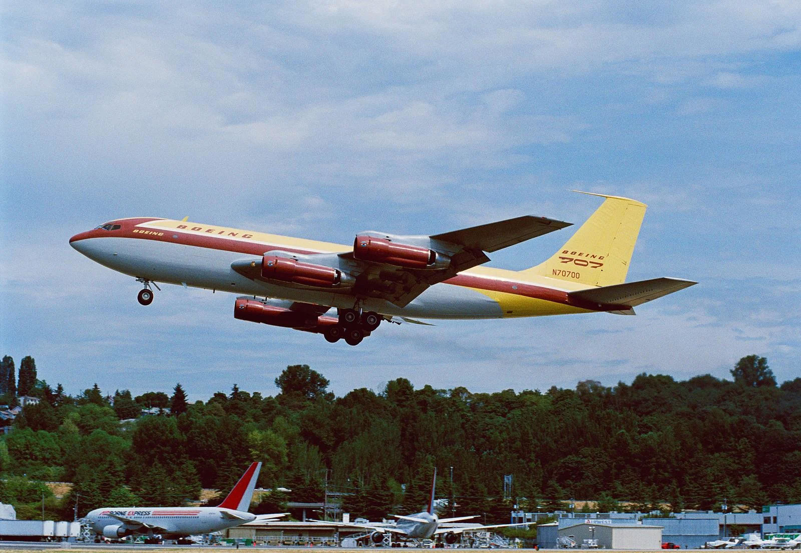 A color photo of the first Boeing 707, a yellow and red commercial jet, taking off.