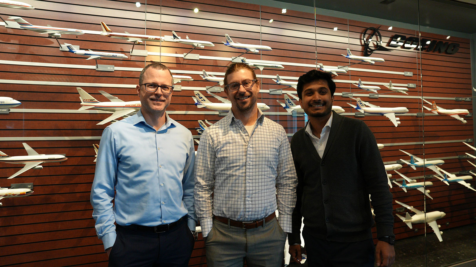 Three engineers stand in front of a wall filled with models of Boeing airplanes