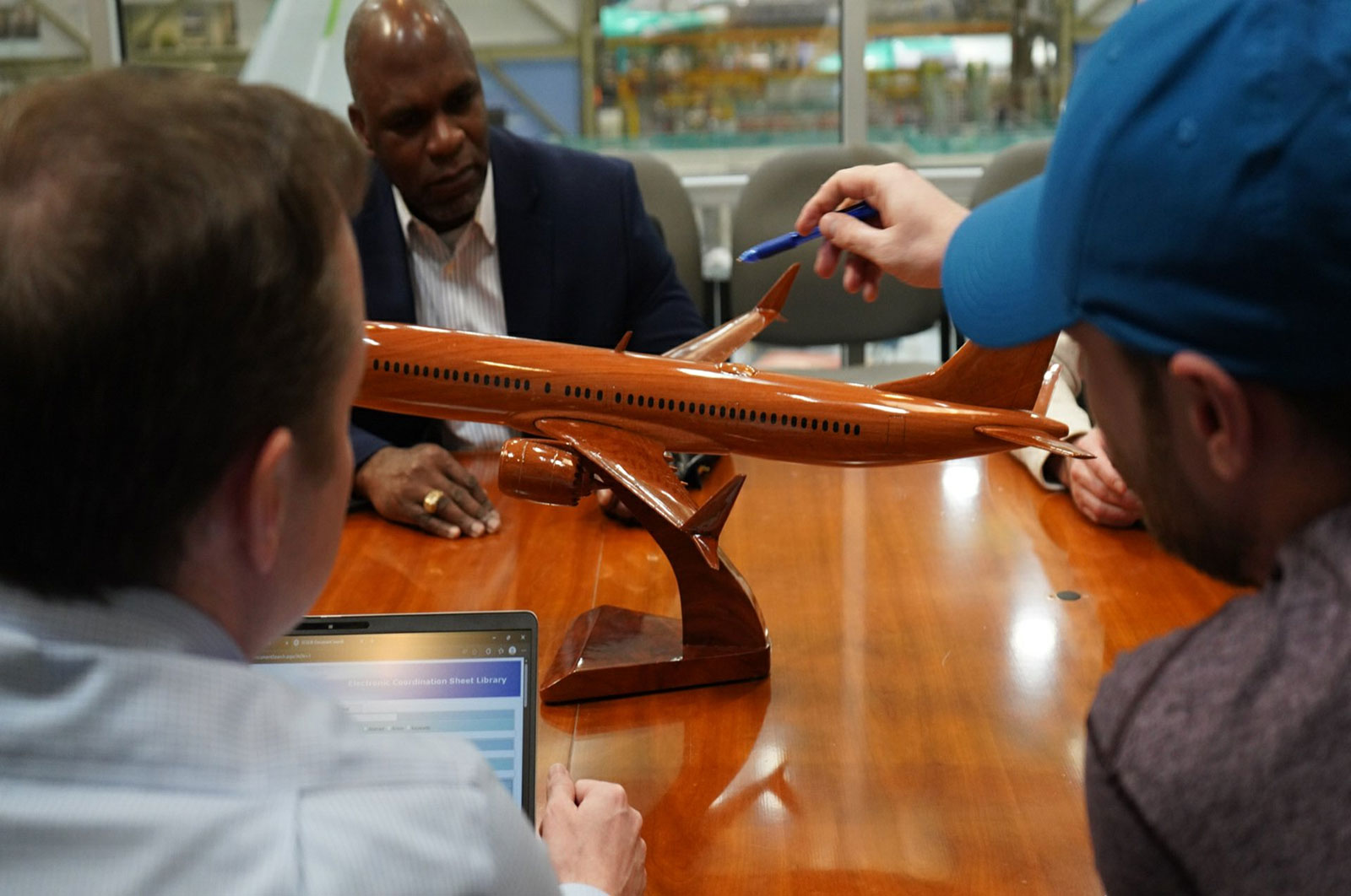 Four engineers sit around a table pointing at a wooden 737 model