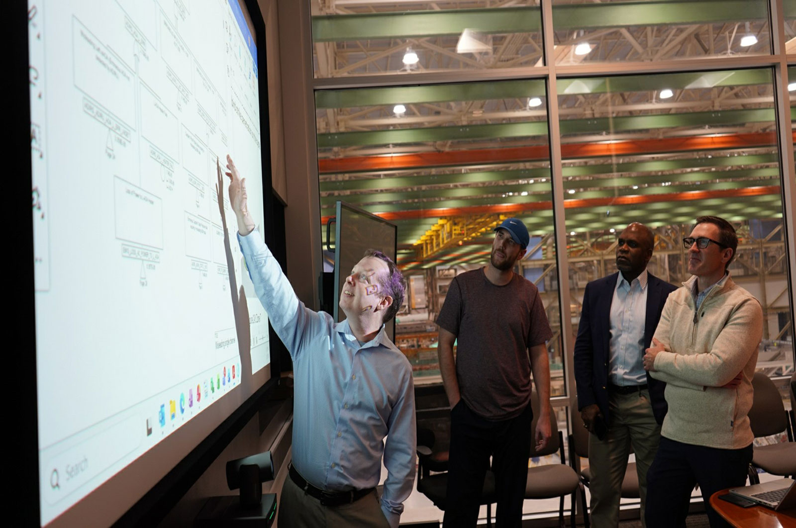 An engineer points at a presentation on a wall inside a factory