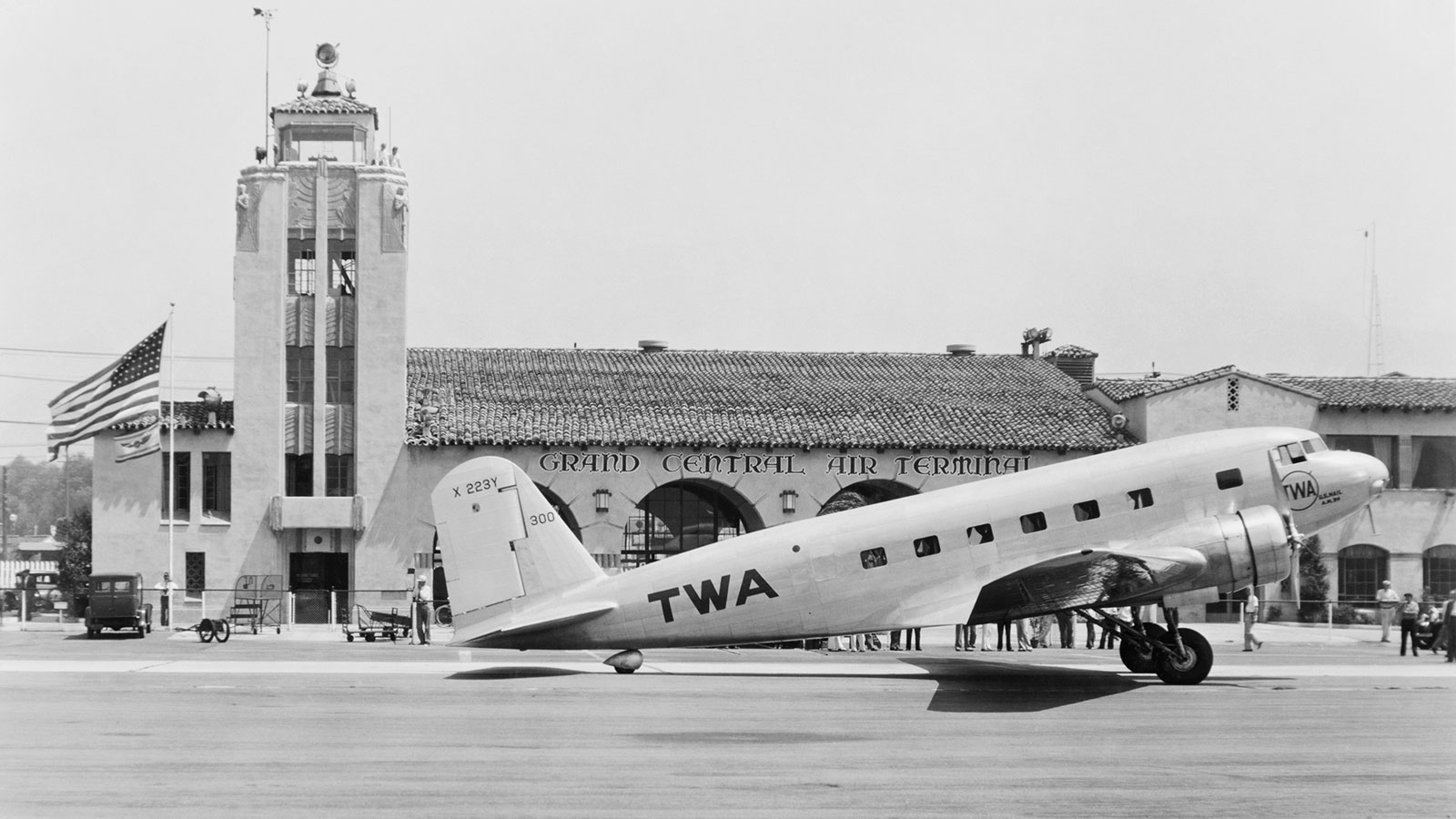 Black and white photo of a DC-1, a two-engine propellor monoplane, on the ground in front of Grand Central Air Terminal in Glendale, CA.