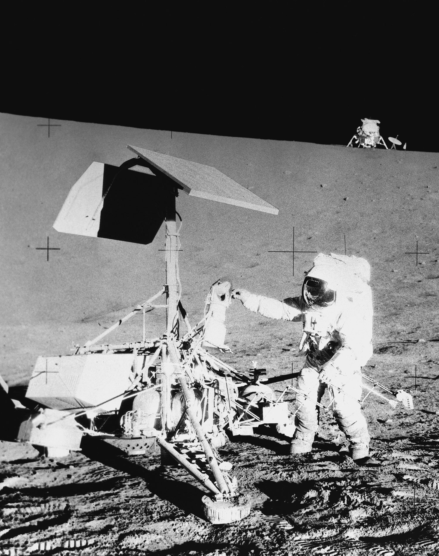 Black and white photo of Surveyor III on the surface of the moon. Astronaut Charles "Pete" Conrad stands next to Surveyor and in the background up on a ridge is the Lunar Lander.