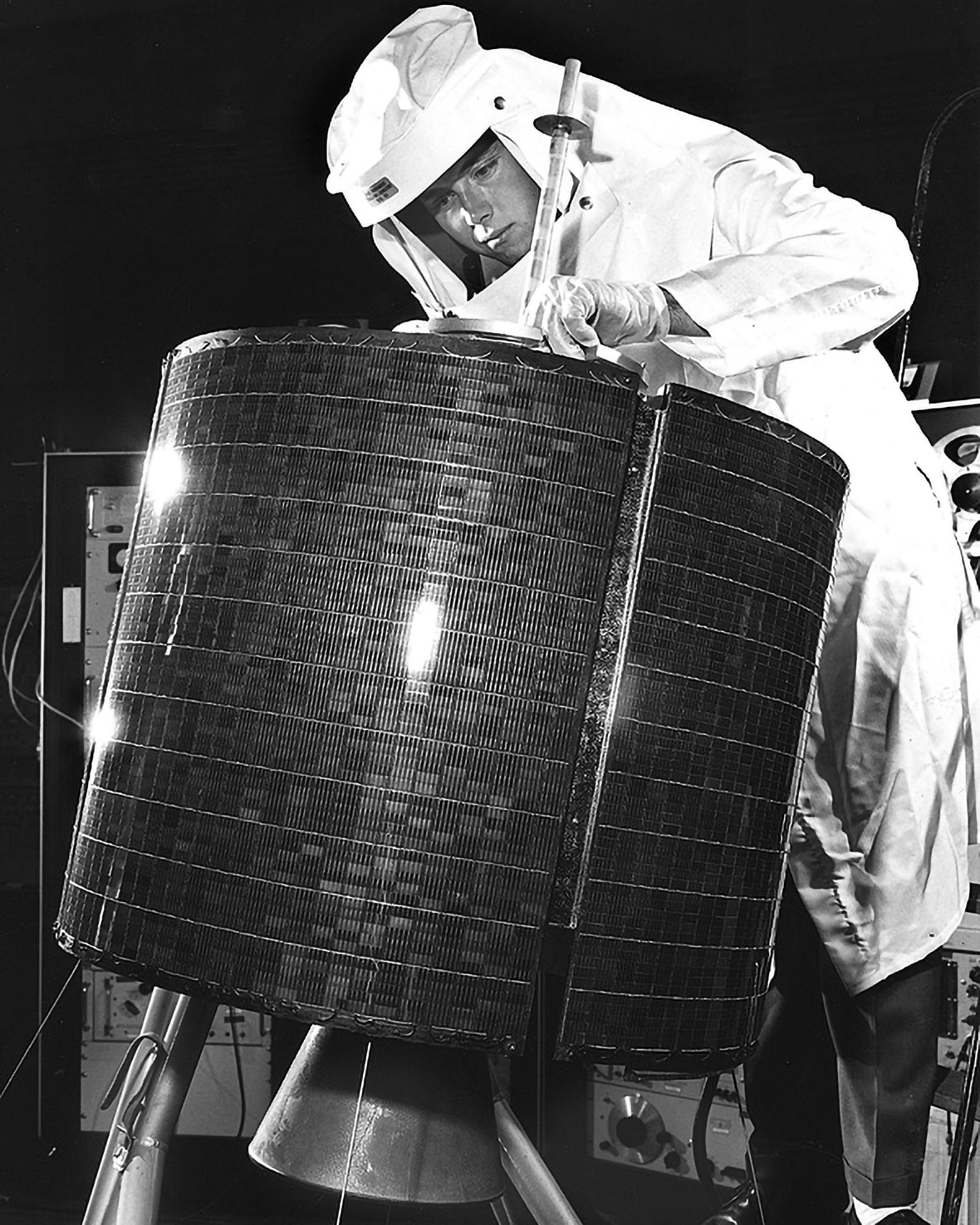 Black and white photo of a worker in protective gear examining the Early Bird satellite