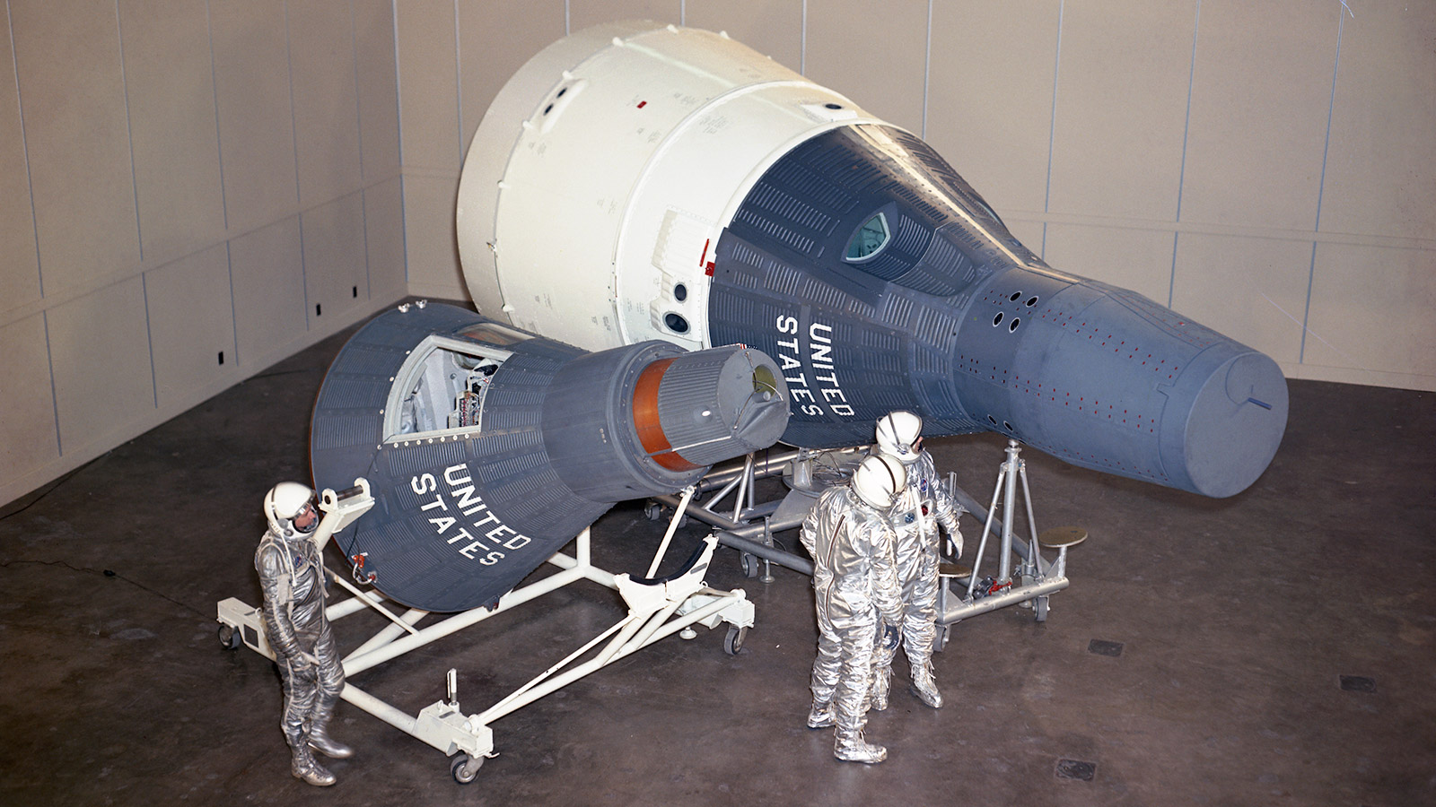 color photo of men in space suits working on an early space craft