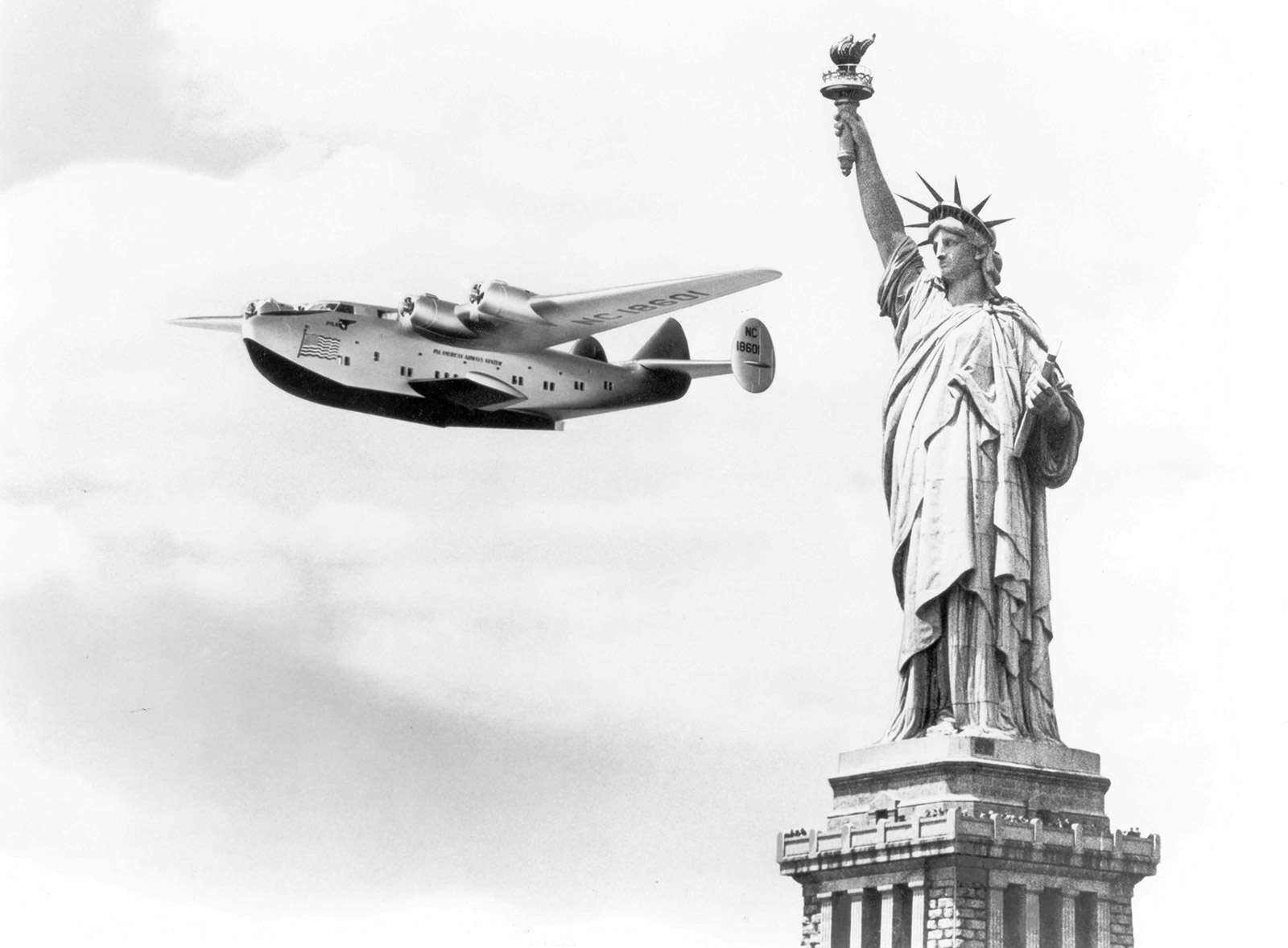 Black and white photo of plane flying by Statue of Liberty