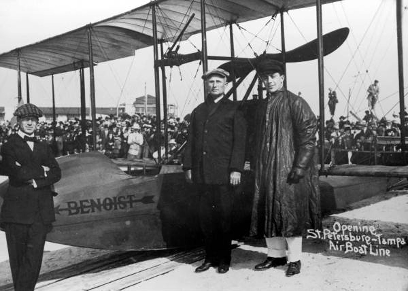 black and white photo of men standing by old bi-plane
