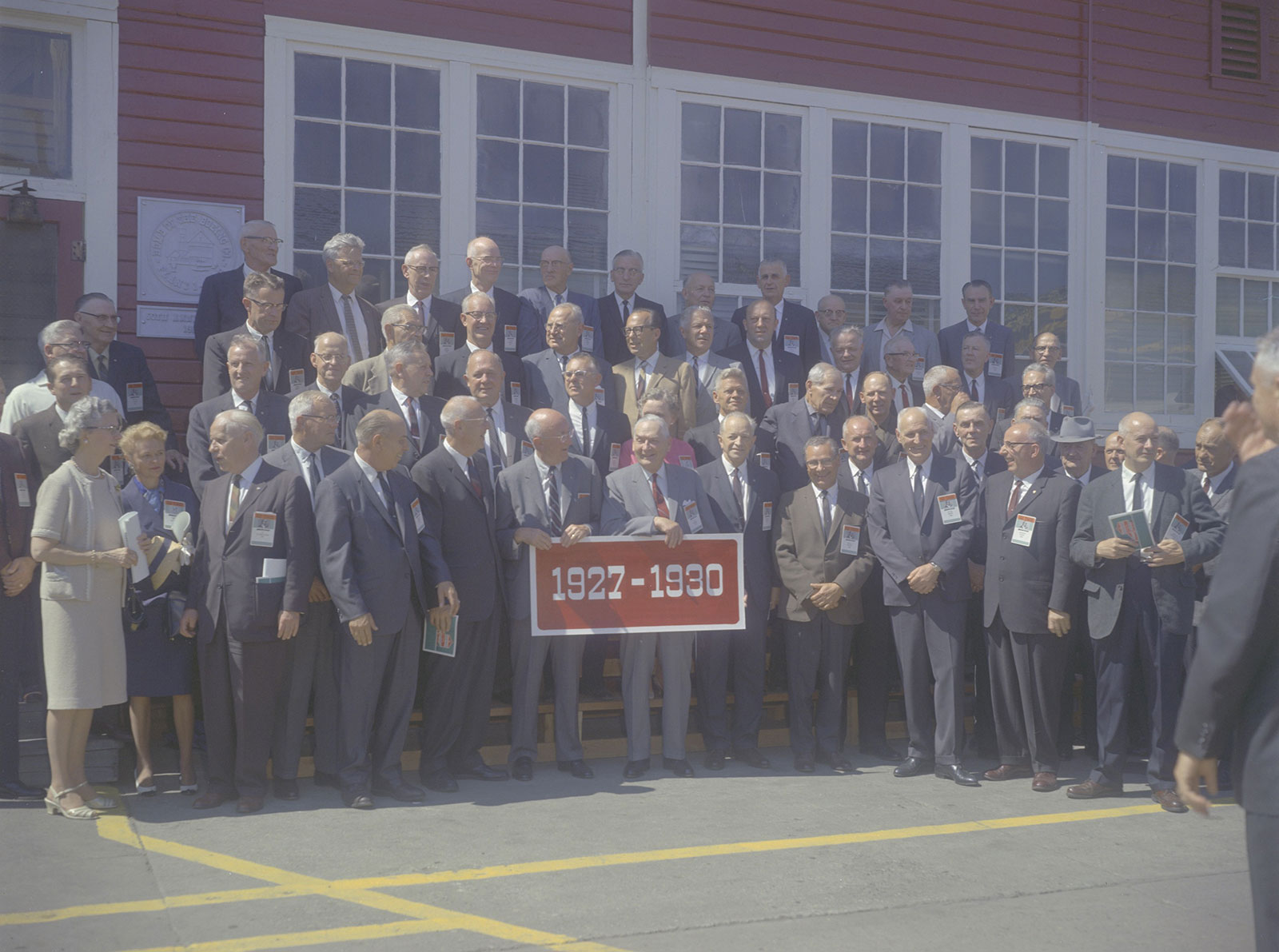 Color photo of a group standing in front of red barn holding a sign