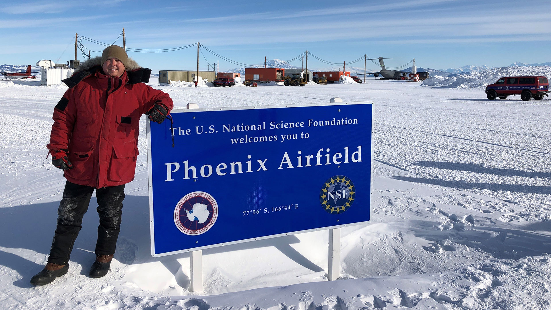 Travis Snyder poses in front of a sign in Antarctica.