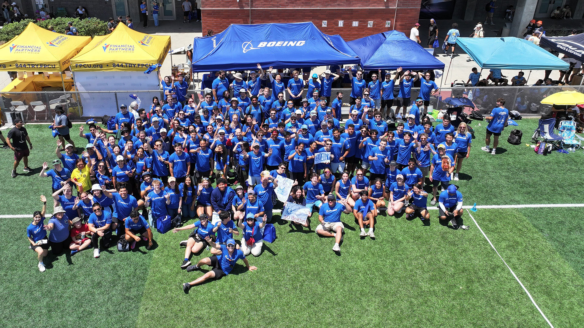 Men and women smiling in a large group near yellow and blue tents.
