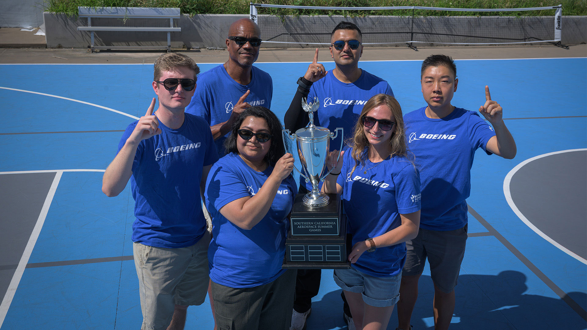 Men and women smiling and holding a first place trophy on blue basketball court.