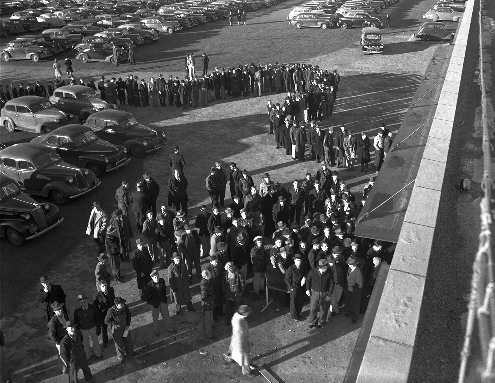 A black and white photo of a group of employees standing outside an airplane factory waiting to get inside.