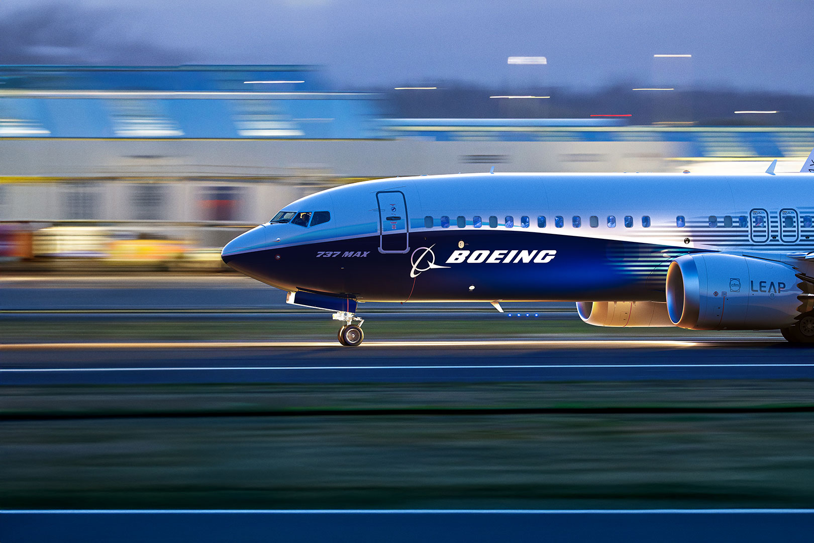 A Boeing 737 MAX lands on an airport runway. The plane is clear and in focus while everything around it is blurred and in motion-- a style of photo editing used to make the airplane stand out.