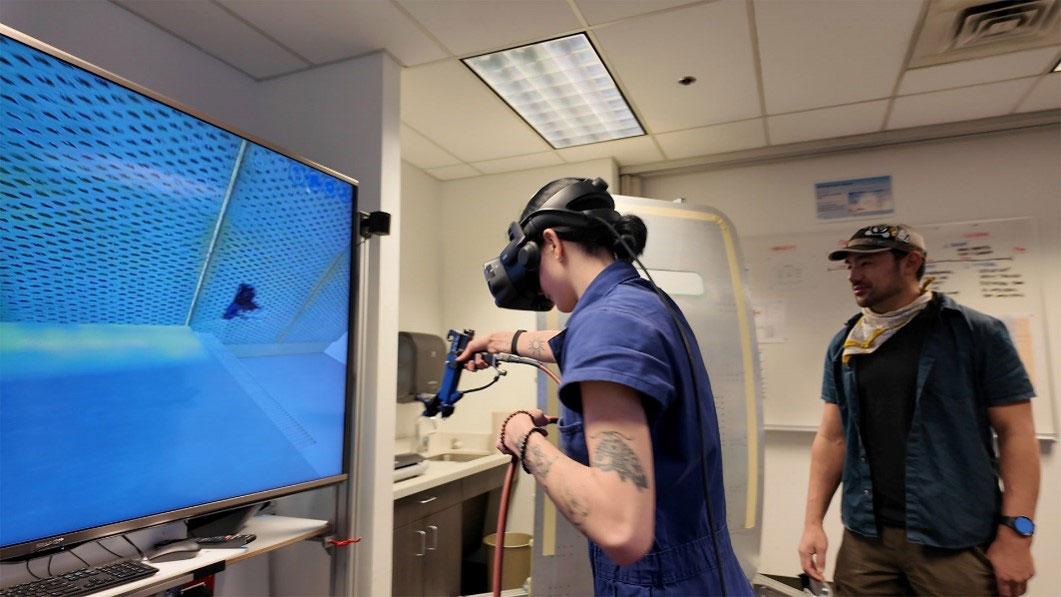 Person using a VR headset to practice spray‑painting while an instructor observes.