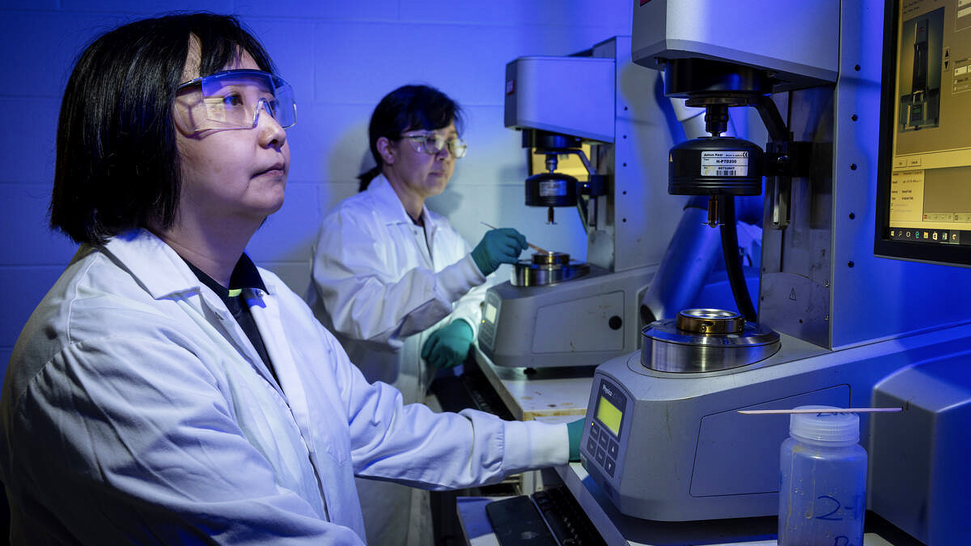 two people examine samples under microscope
