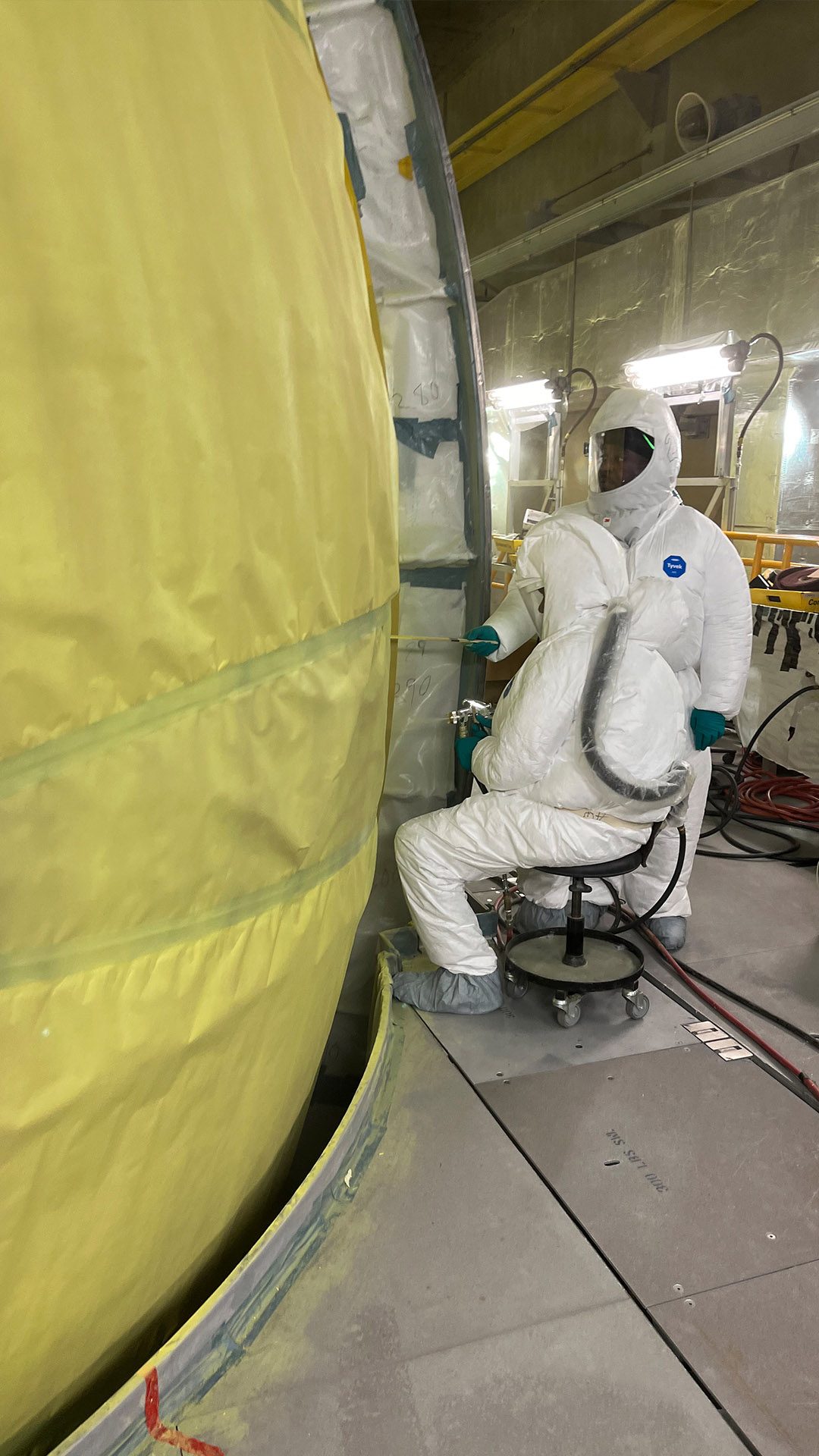 two people in protective gear test a spraying device on fuel tank dome