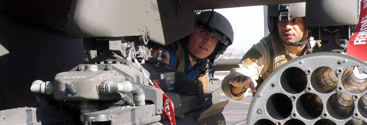 Two people in military helmets adn gear inspect a defense product