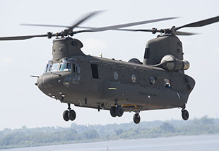 Side view of a Chinook Block 2 hovering over water and trees.