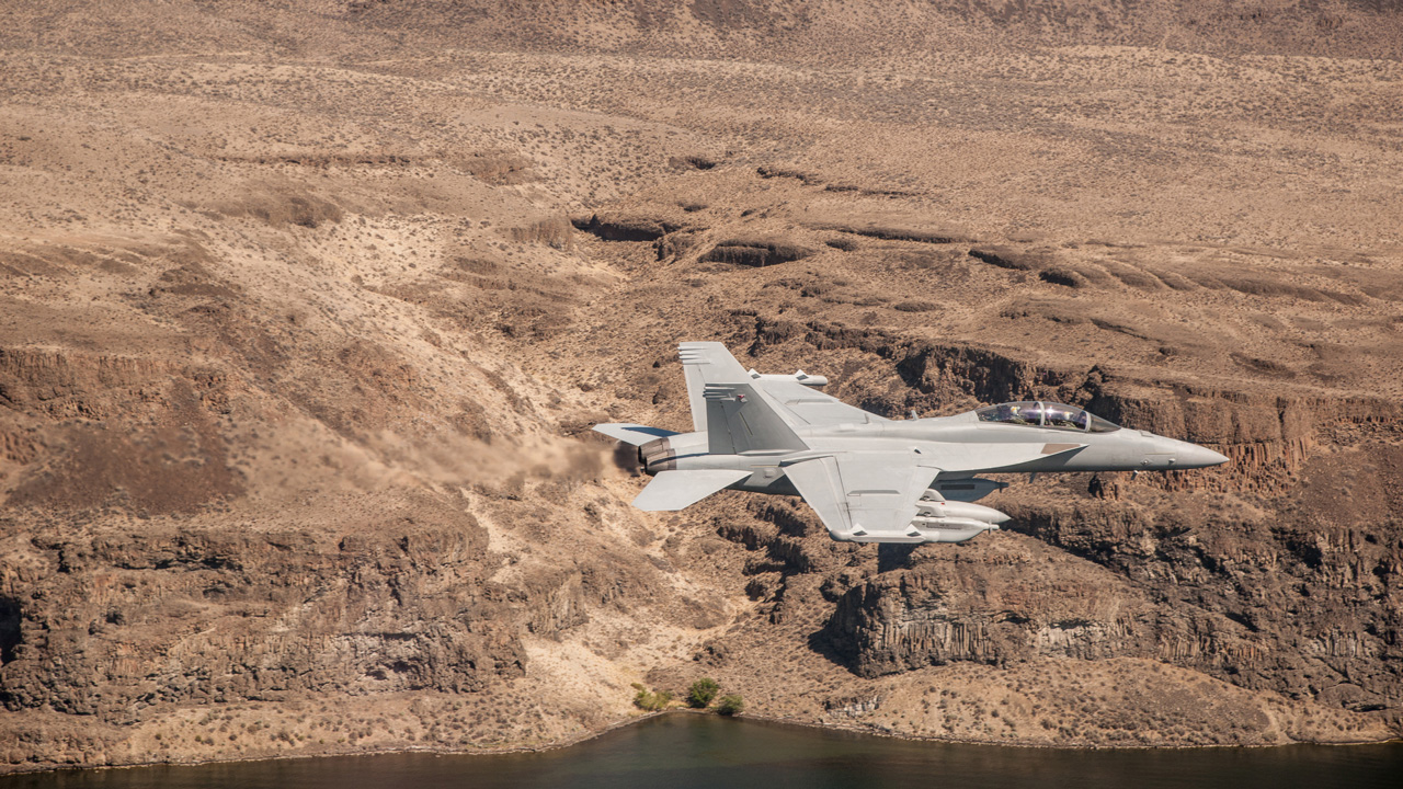 EA-18G Growler aircraft in flight over desert terrain and water.