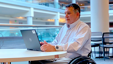 man in wheelchair sitting at desk working on laptop