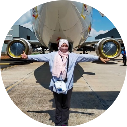 Vini Maskun in front of a plane with her arms out.