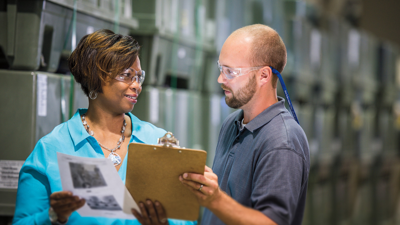 Main image showing a woman and man in discussion, each with safety glasses on, clipboard in hand.