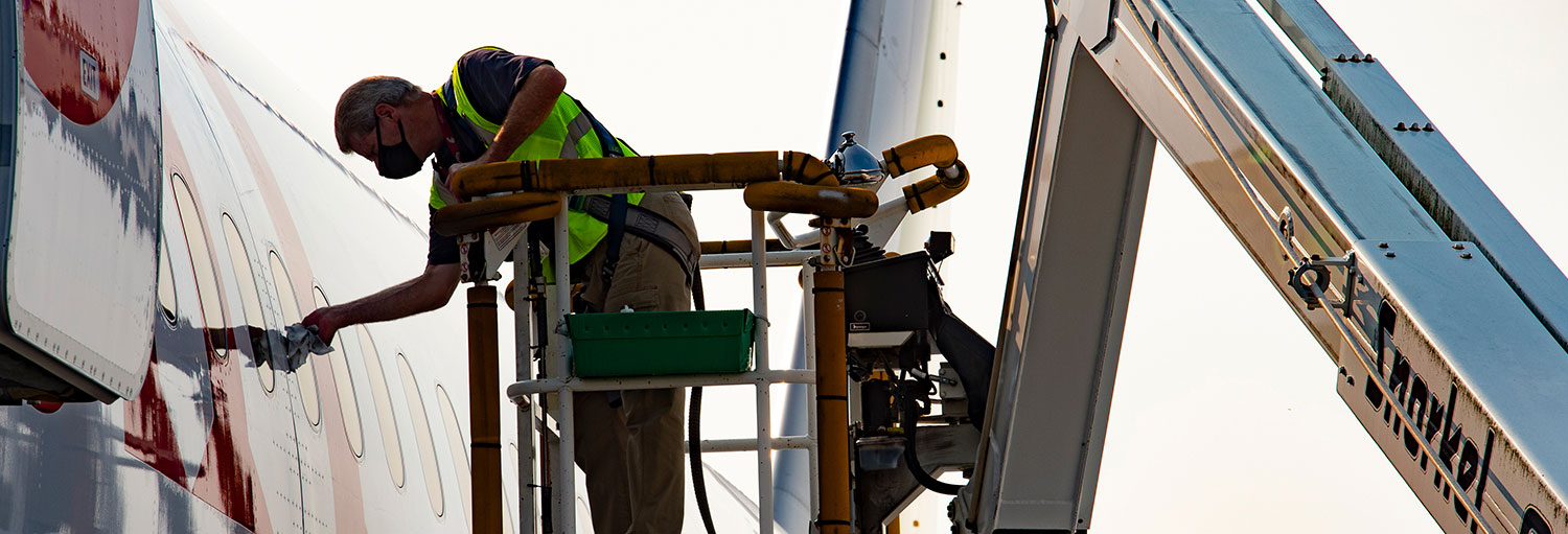 Two employees in safety gear working on the underside of an airplane.