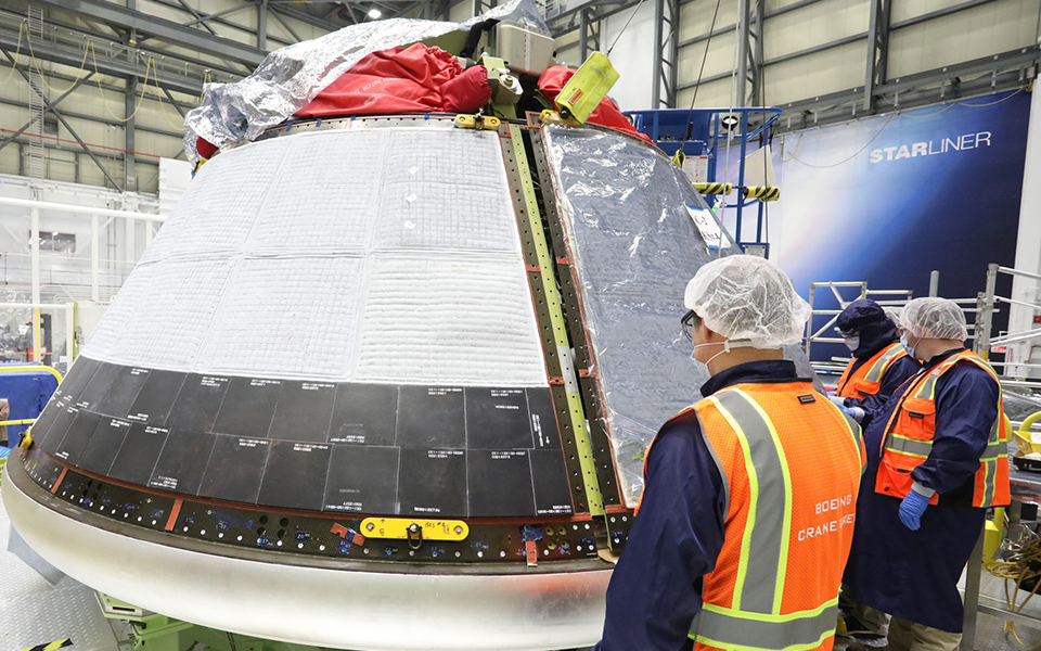 Picture of Boeing technicians installing the backshells on the Orbital Flight Test 2 Crew Module.